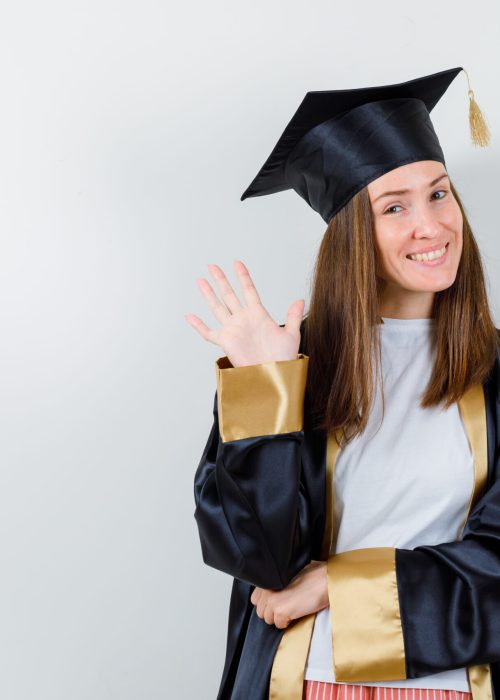 female graduate in uniform, casual clothes waving hand to say goodbye and looking merry , front view.